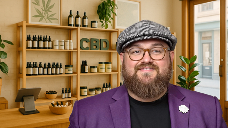 Yorkshire Bob, Northern Payments' company mascot, standing in a CBD store wearing a purple blazer and flat cap with CBD products in the background